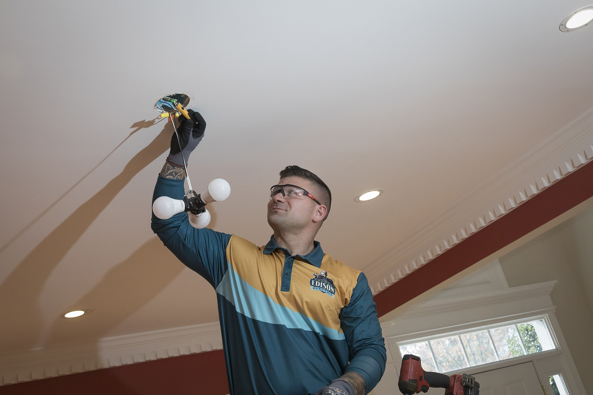 Electrician installing a ceiling light fixture in a home.