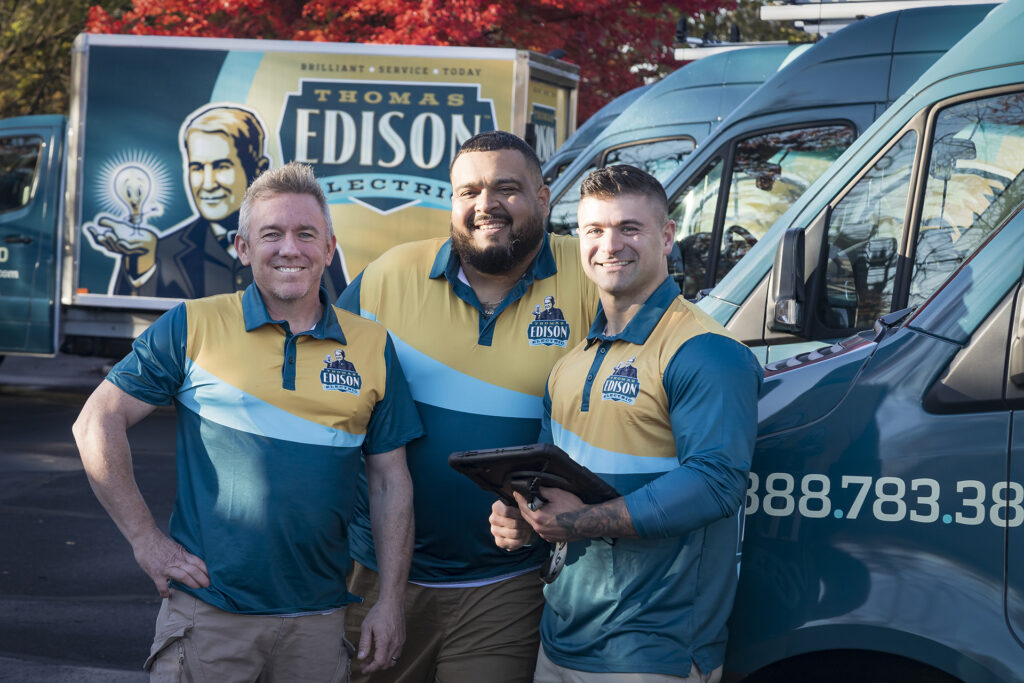 Thomas Edison Electric team of electricians standing beside company vans.