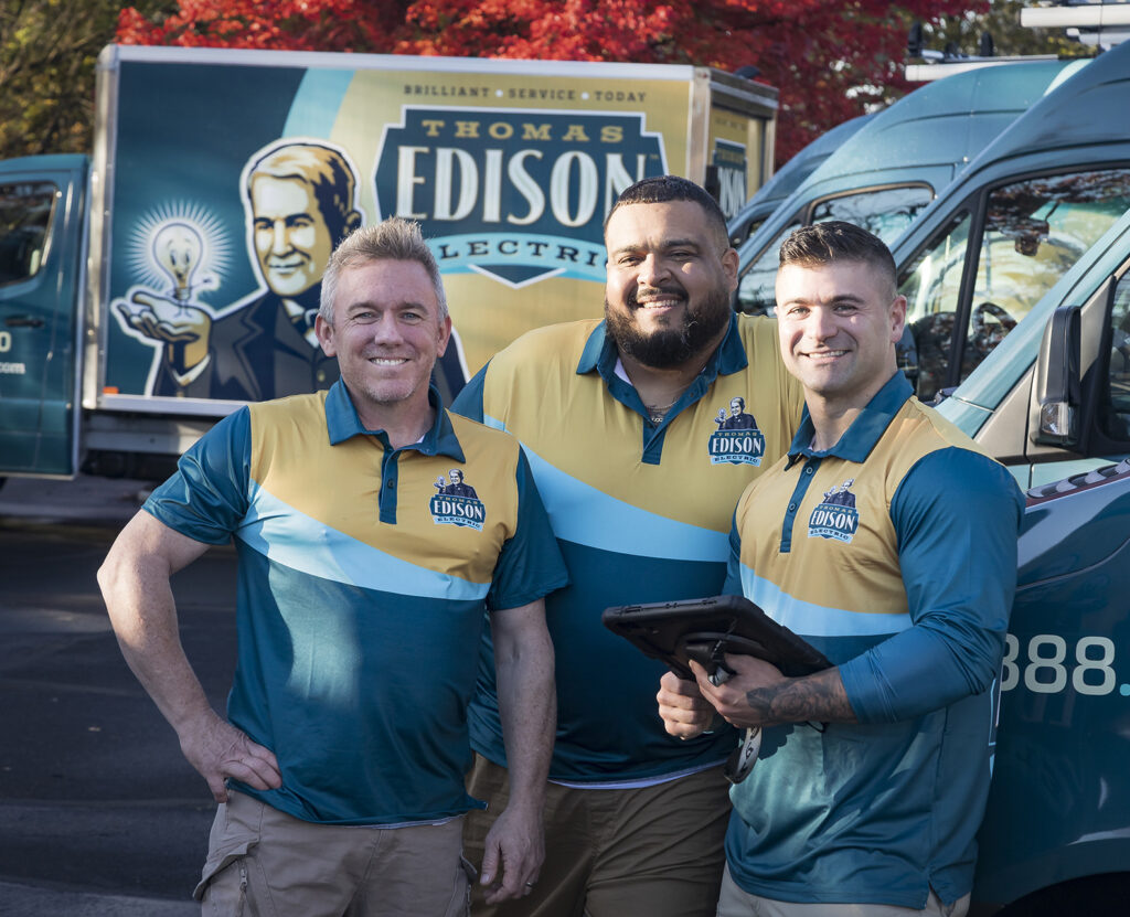 Thomas Edison Electric team of electricians standing beside company vans.