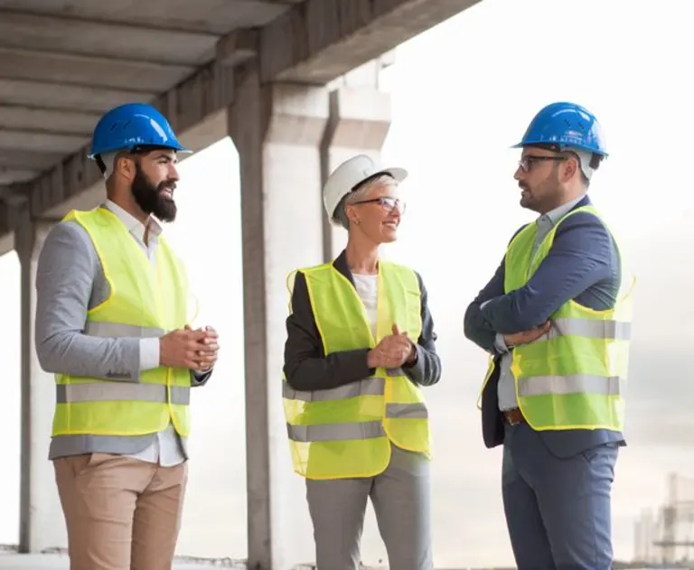 This image depicts a team of construction professionals, including an architect and civil engineers, engaging in a site meeting to discuss project management and infrastructure development.