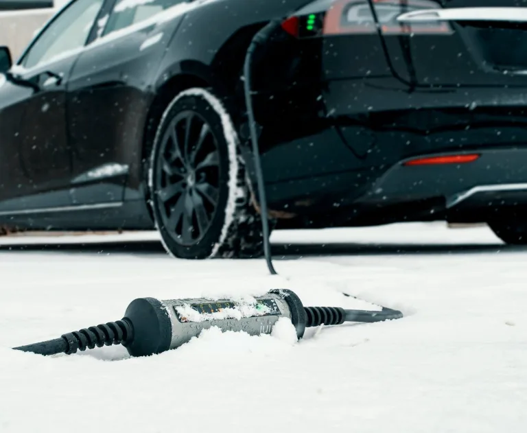 The image displays a Tesla vehicle being charged in snowy conditions.