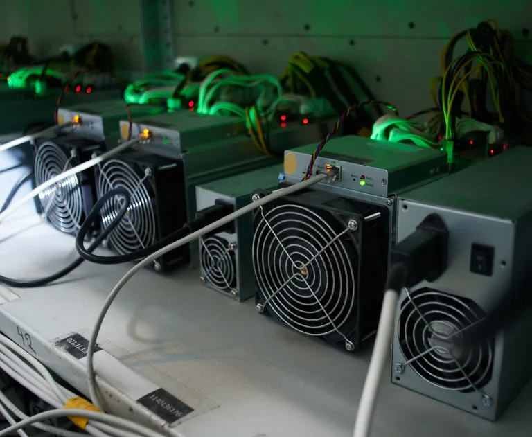 The image displays a row of Antminer Bitcoin mining machines, which are specialized hardware designed for cryptocurrency mining.
