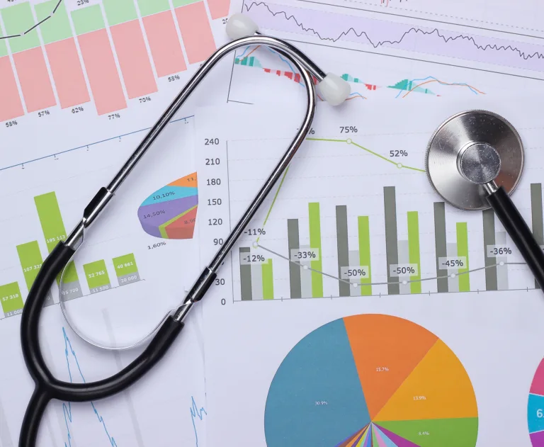 The image displays medical financial analytics data, featuring a stethoscope placed over various charts and graphs.