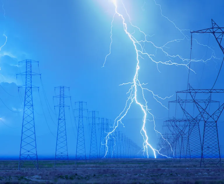 This image depicts a lightning strike occurring near high-voltage power lines and transmission towers, showcasing a significant weather event affecting electrical infrastructure.