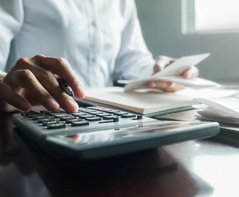This image depicts a person performing financial calculations using a desktop calculator and reviewing documents.