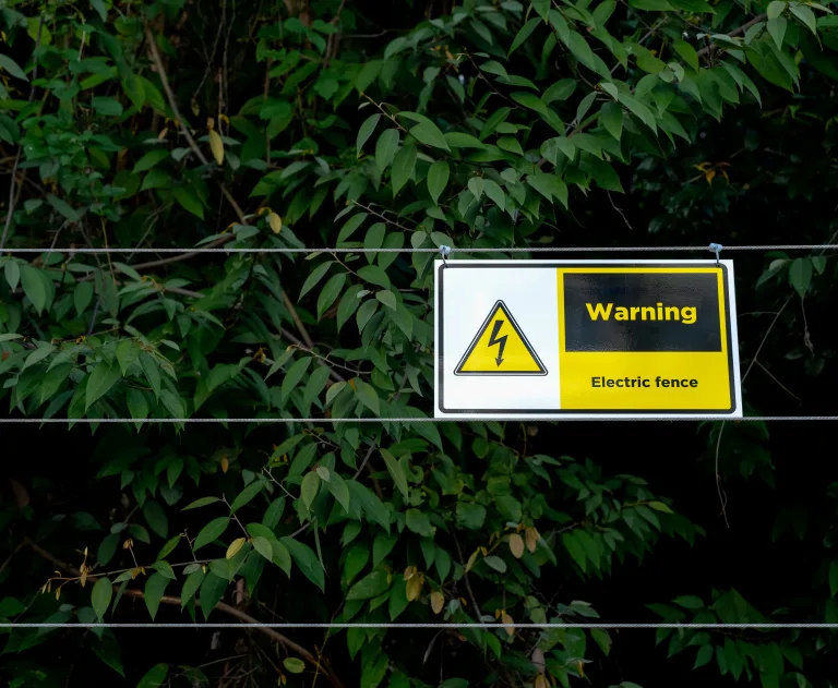 The image displays a warning sign installed on an electric fence to alert people and animals to potential danger.