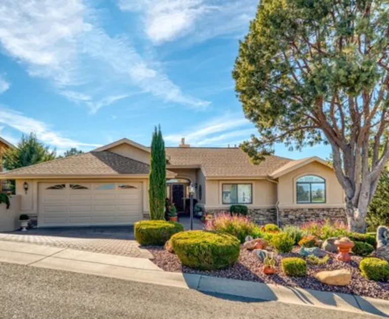 This image shows a tan colored home with many plants well maintained plants in the front yard.