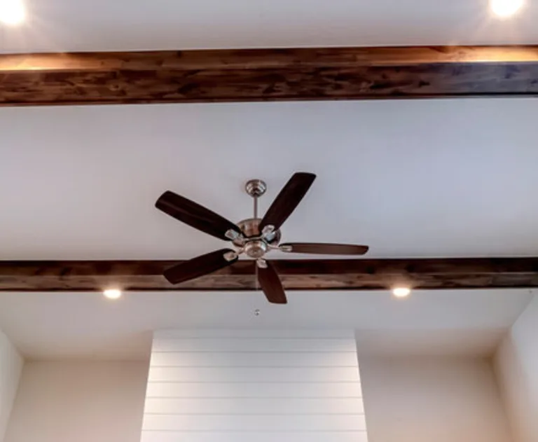 A ceiling fan with lights between the decorative wooden beams inside the living room of a home.