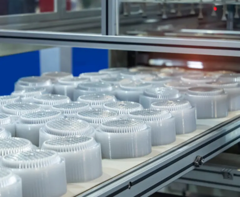 A stack of polypropylene food containers on a conveyer belt of an automatic plastic injection molding machine.
