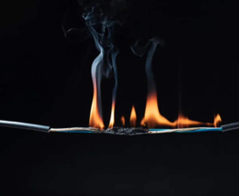 The image displays a dangerous electrical hazard caused by burning electrical wire, likely due to a short circuit or severe overloading.