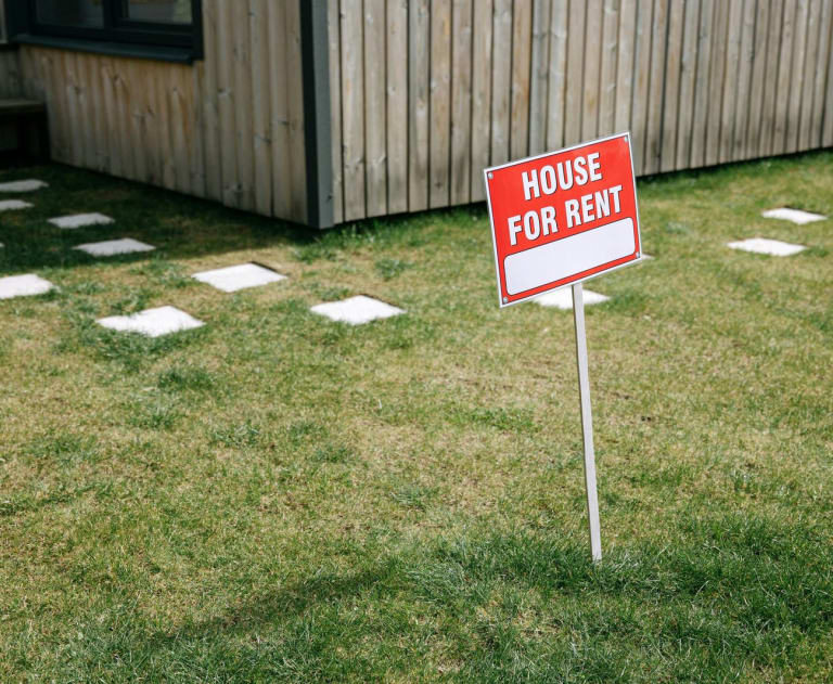 This image shows a "House for Rent" sign placed on a residential lawn, indicating that the property is available for lease.