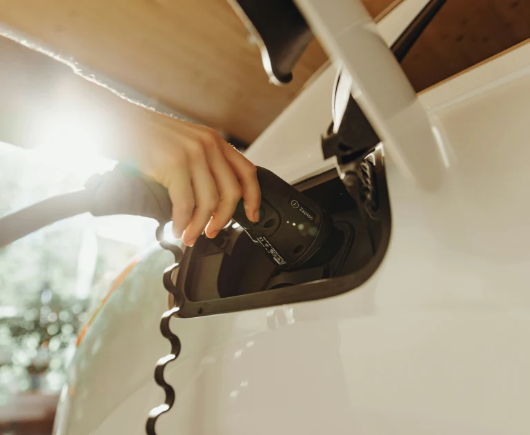 A person charging their electronic vehicle, with the angle close up on the hand and the charger.