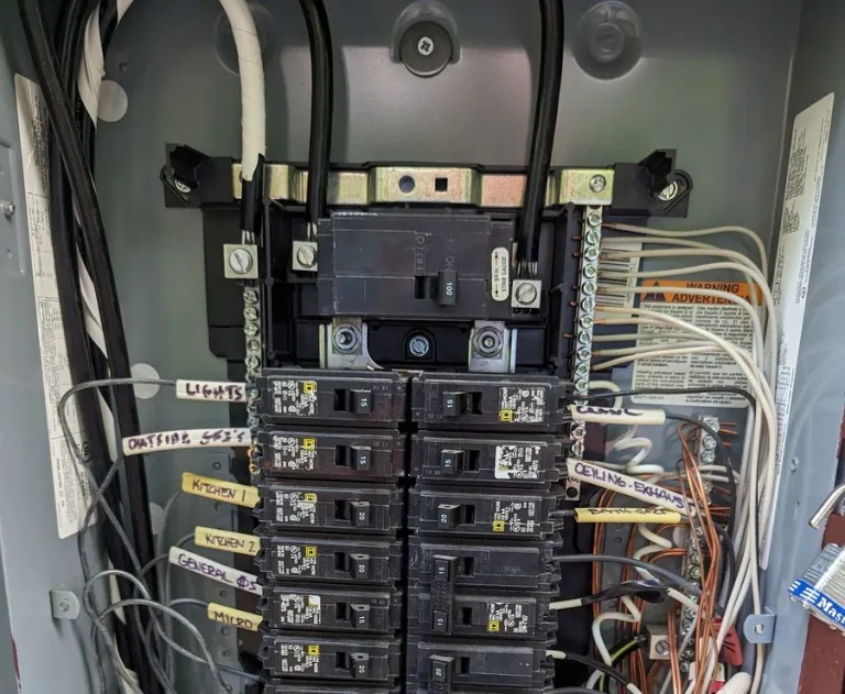 The image displays an electrical load center or breaker panel, specifically a Square D Homeline model. This panel safely distributes electricity throughout a building and protects circuits from overloading or short-circuiting.