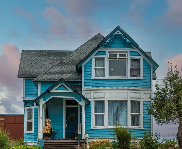 This image is a stock photo of a historic blue Victorian house, often depicted on a hill. It features classic Victorian-era architecture with a front porch, ornate details, and steep rooflines.