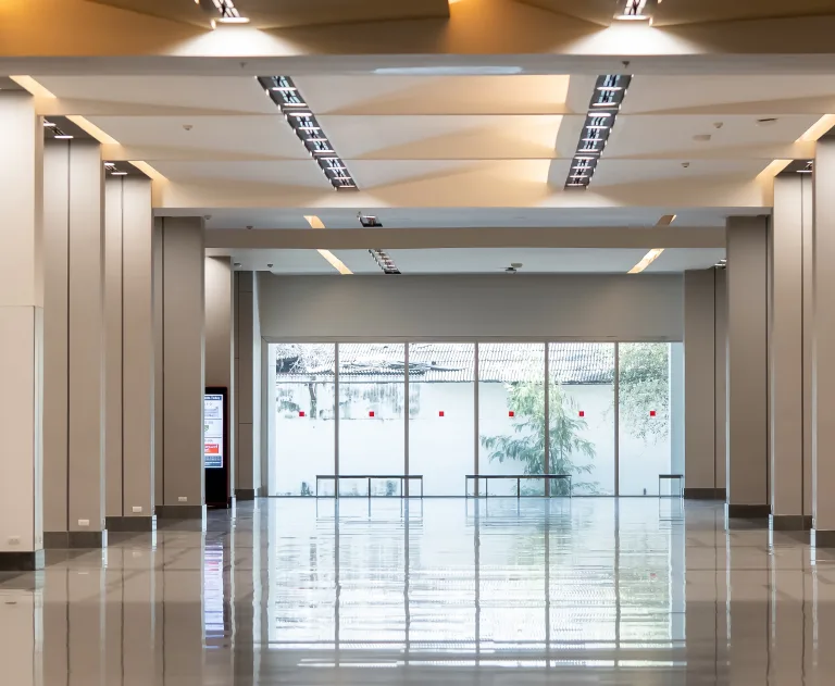 This image shows a spacious modern commercial lobby or terminal featuring large windows, polished reflective floors, and structured ceiling lighting.