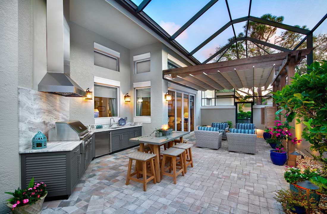This image features a modern, screened-in outdoor kitchen and living area, complete with a built-in grill station, cabinetry, and a dining table in Florida.