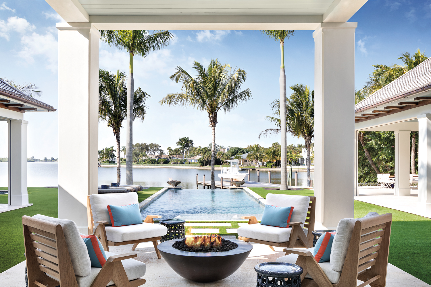 The image features a luxurious coastal Florida home designed by John M. Brenner, which includes a central covered loggia equipped with Sutherland's Cat's Cradle lounge chairs and an outdoor fire pit.