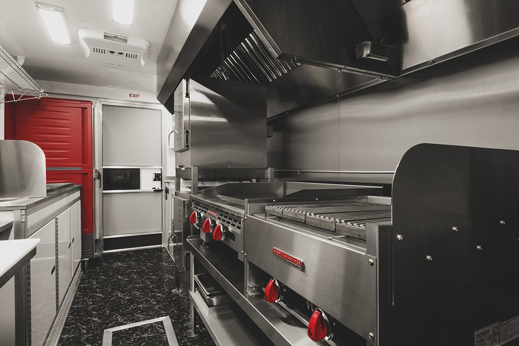 This is a custom-built, stainless steel commercial food truck interior. Key features of this mobile kitchen include a griddle, char broiler, and overhead exhaust hood.