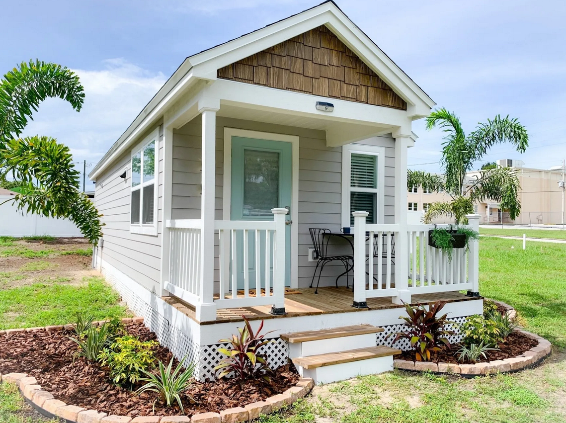 This image features a modern tiny house situated on a foundation, likely in Florida based on the palm trees and architectural style.