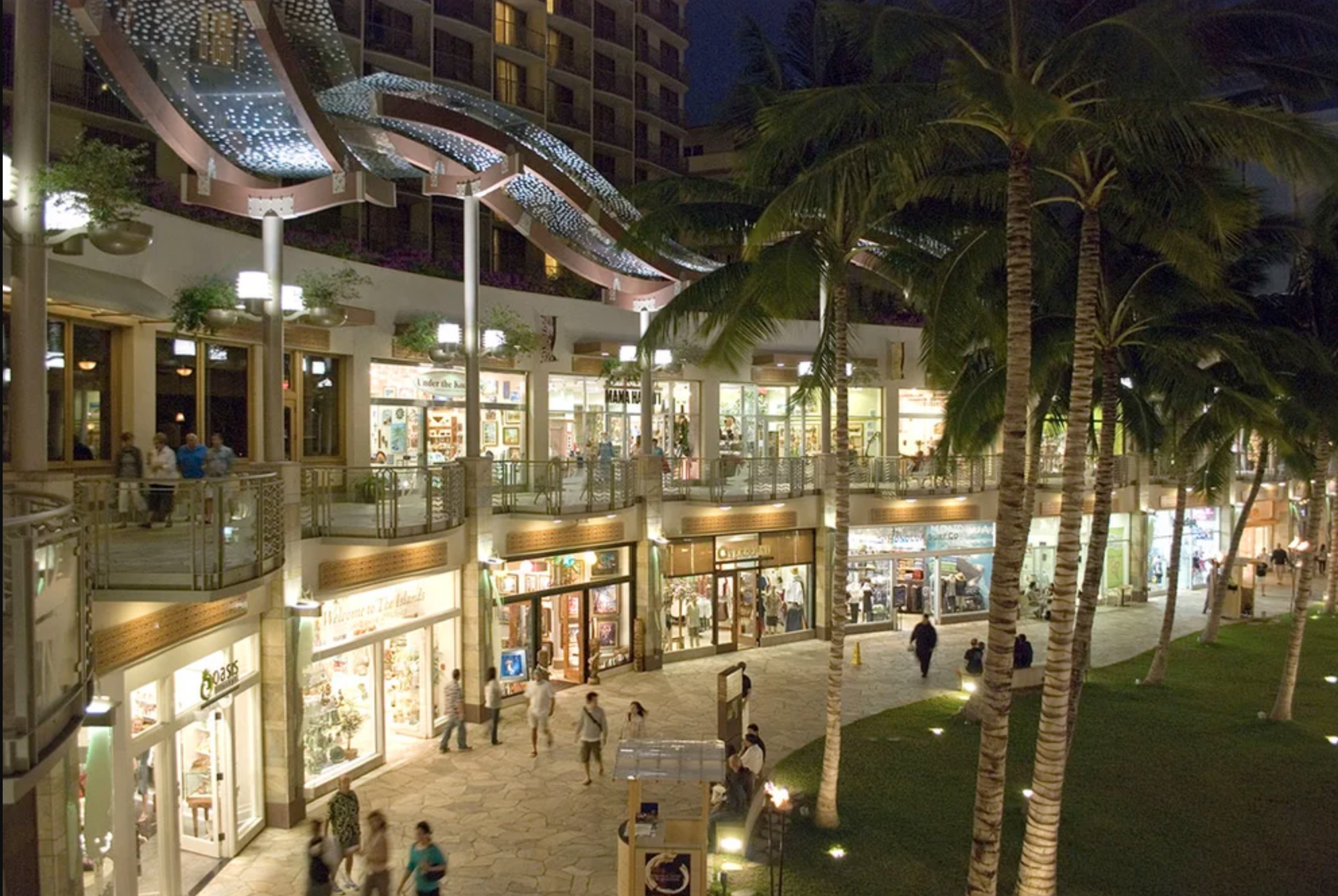 This image shows a vibrant shopping center at night with palm trees and bright lighting.
