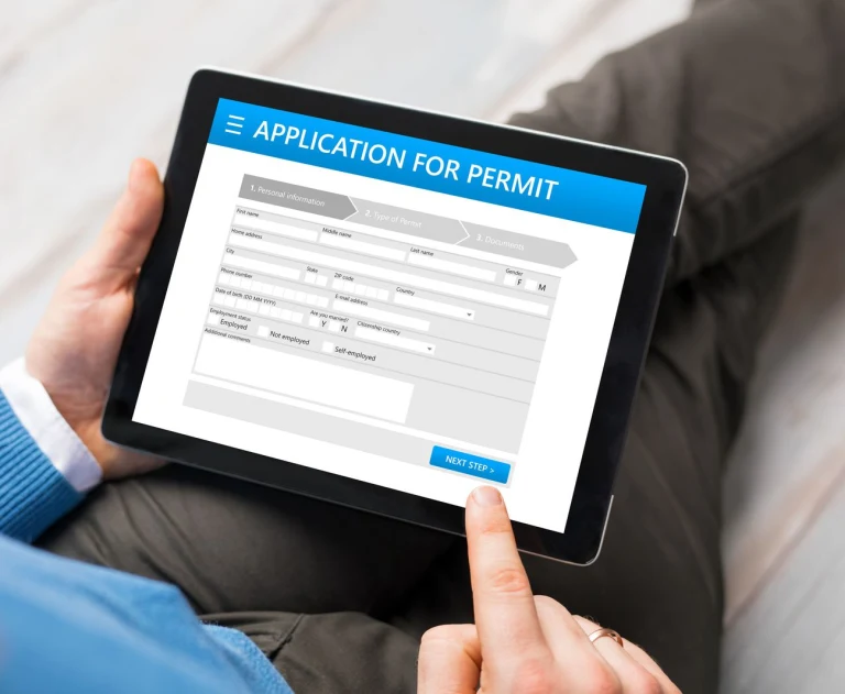 This image shows a person filling out an online "APPLICATION FOR PERMIT" form on a tablet device.