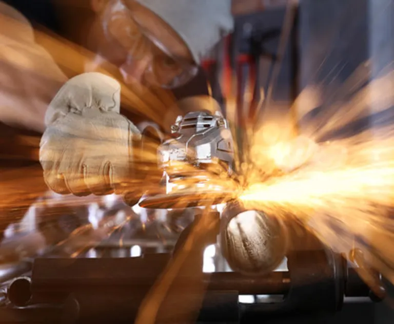 This image shows a person using an angle grinder to cut or grind a metal pipe, producing a shower of sparks, like what you'd find in a specialty workshop.