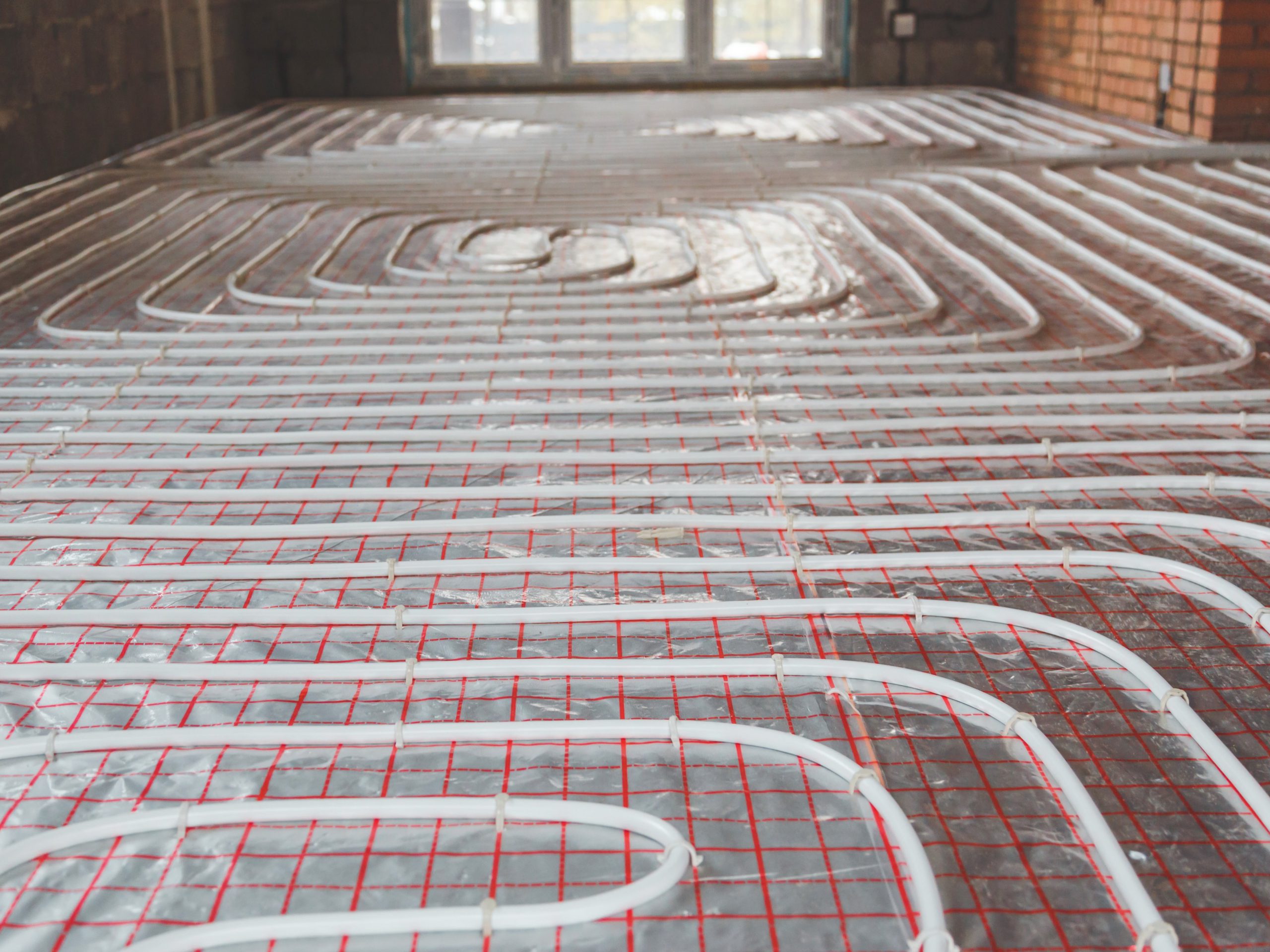 This image shows a hydronic underfloor heating system being installed. This system uses plastic tubing to circulate hot water beneath the floor surface to provide heat.