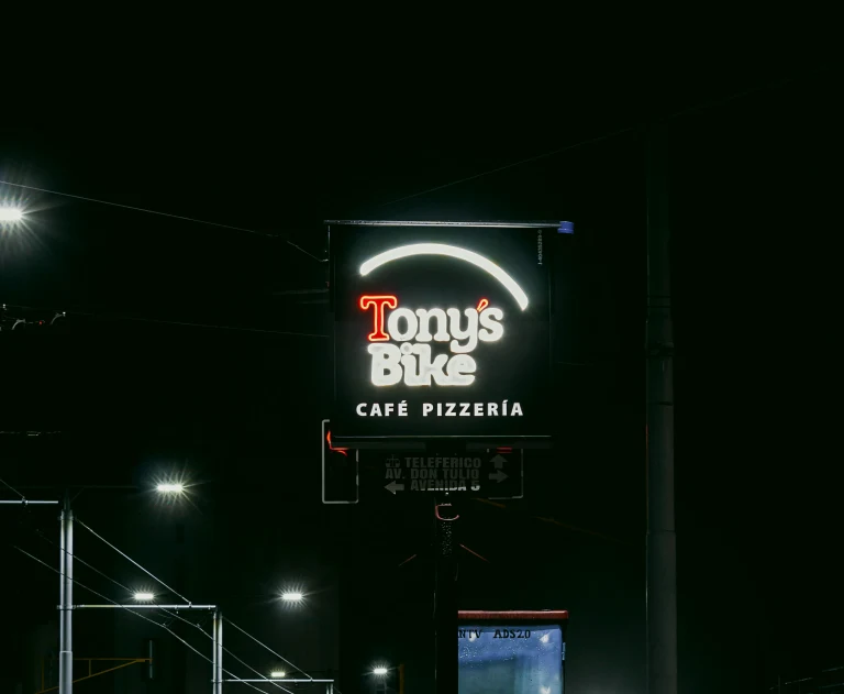 This image features a glowing neon sign for a business named Tony's Bike Café Pizzeria at night.