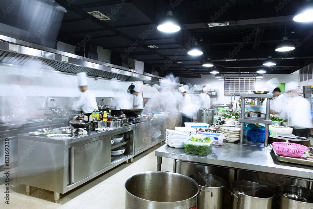 The image depicts a busy, modern commercial hotel kitchen with chefs preparing food.