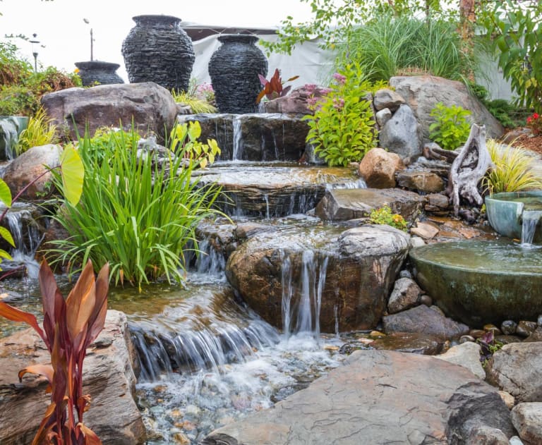 This image shows a professionally landscaped backyard water feature, likely a pondless waterfall designed for serene outdoor living.
