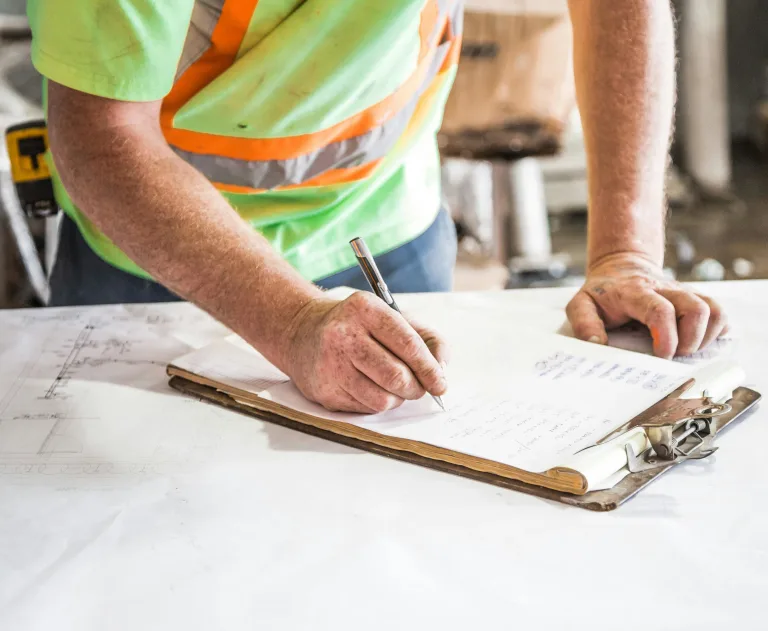 This image depicts a construction worker reviewing plans on a clipboard.