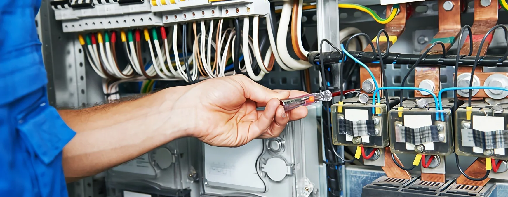 This image depicts an electrician working on a complex electrical panel, likely performing installation, maintenance, or troubleshooting.