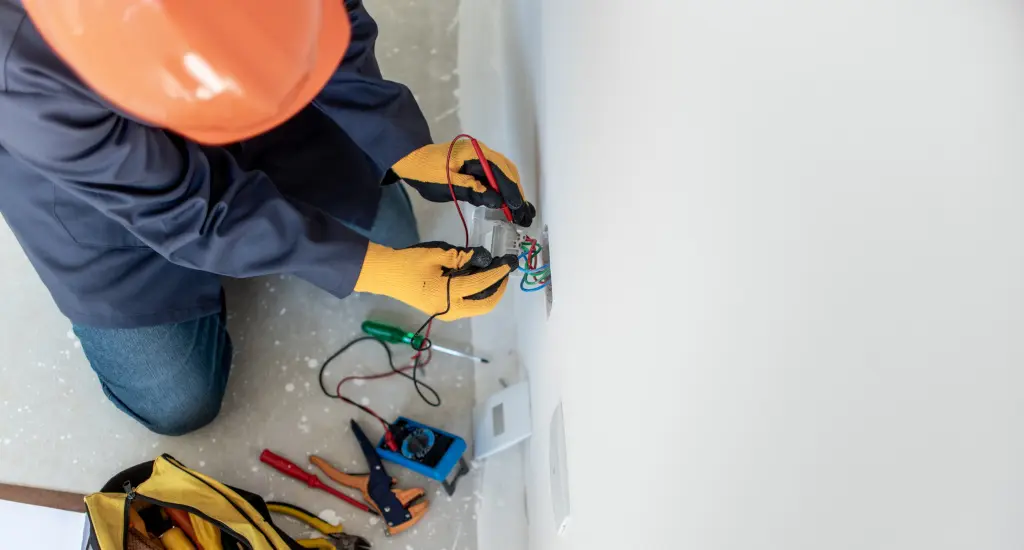 This image depicts a professional electrician installing or repairing electrical wiring for a wall outlet.