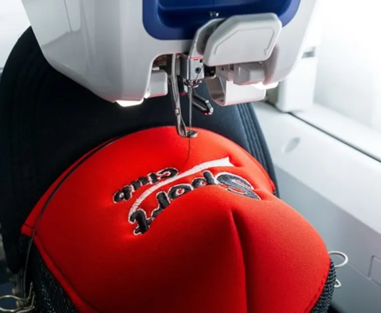 This is an industrial embroidery machine performing custom embroidery on a red baseball cap.
