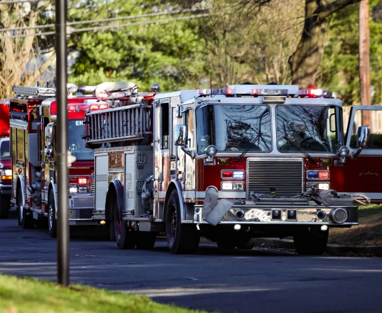 This image displays two red and white fire engines driving down a residential street.