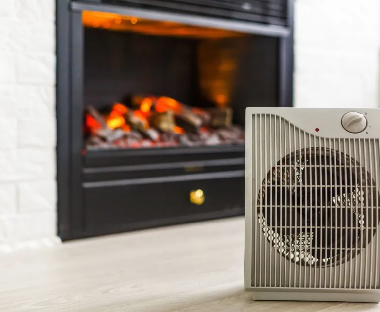 This image displays a portable electric fan heater positioned near an electric fireplace during the winter.