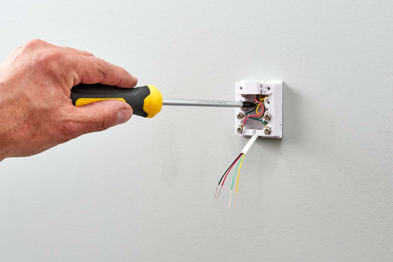 how-to-wire-a-telephone-jack-1152704_03_installmounting_31429-c8757875401f40388555e6ea52c0d6c3 - Thomas Edison Electric The image depicts the installation of a low-voltage communication wall jack, likely for a telephone or data connection, rather than high-voltage electrical wiring.