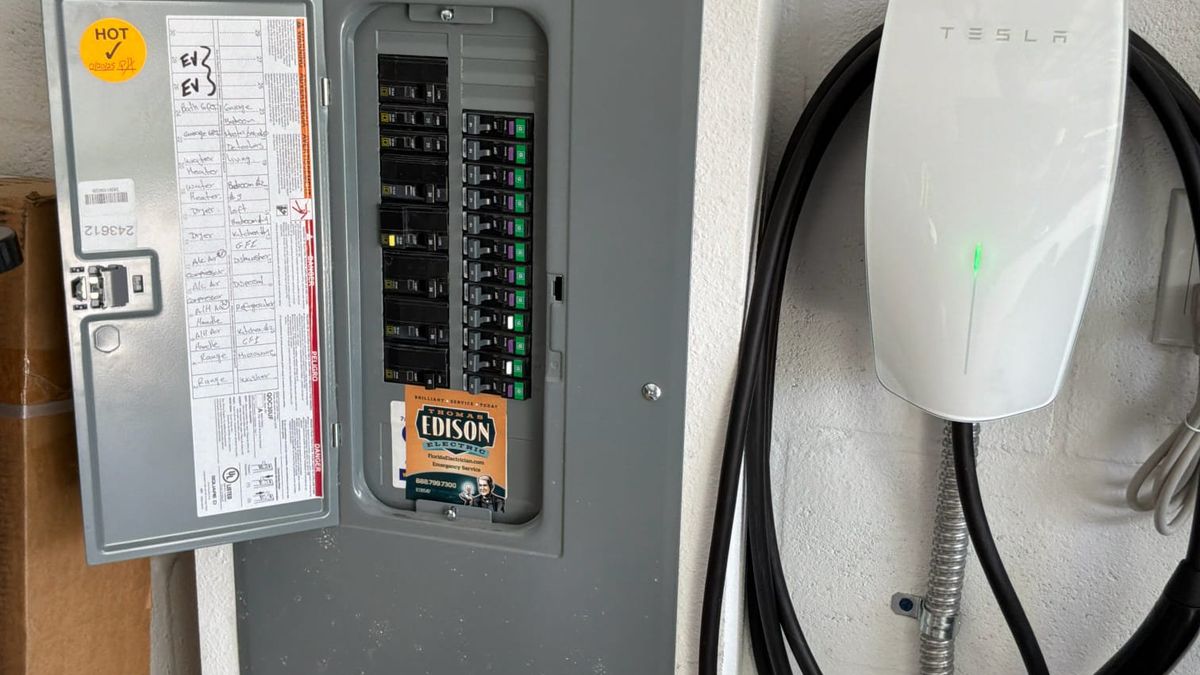 EV charger dedicated circuit in a garage panel, Palm Beach County - Thomas Edison Electric Garage electrical panel with a dedicated EV charger circuit labeled at the top and the wall connector mounted beside it, EV charger installation work in Palm Beach County, Florida