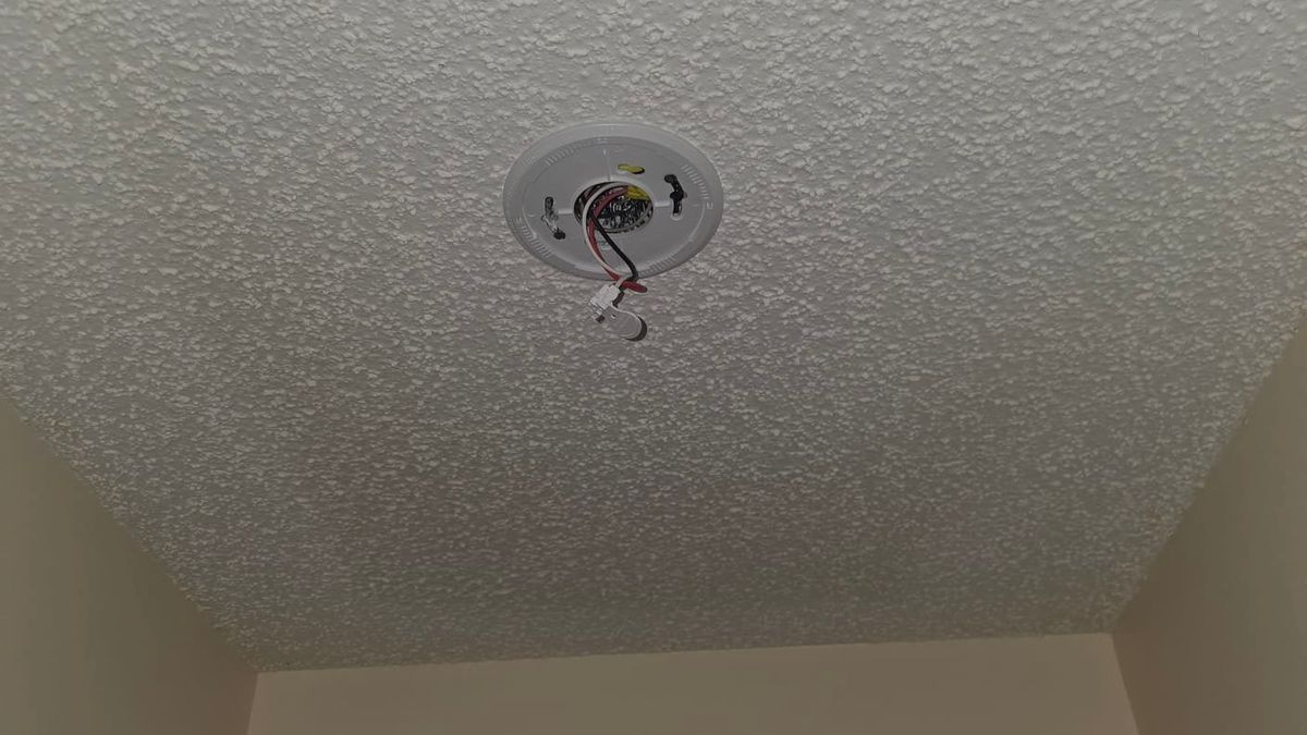 Hardwired smoke alarm mounting plate on a ceiling in a Jupiter, Florida home with the interconnect wiring harness exposed during an alarm replacement