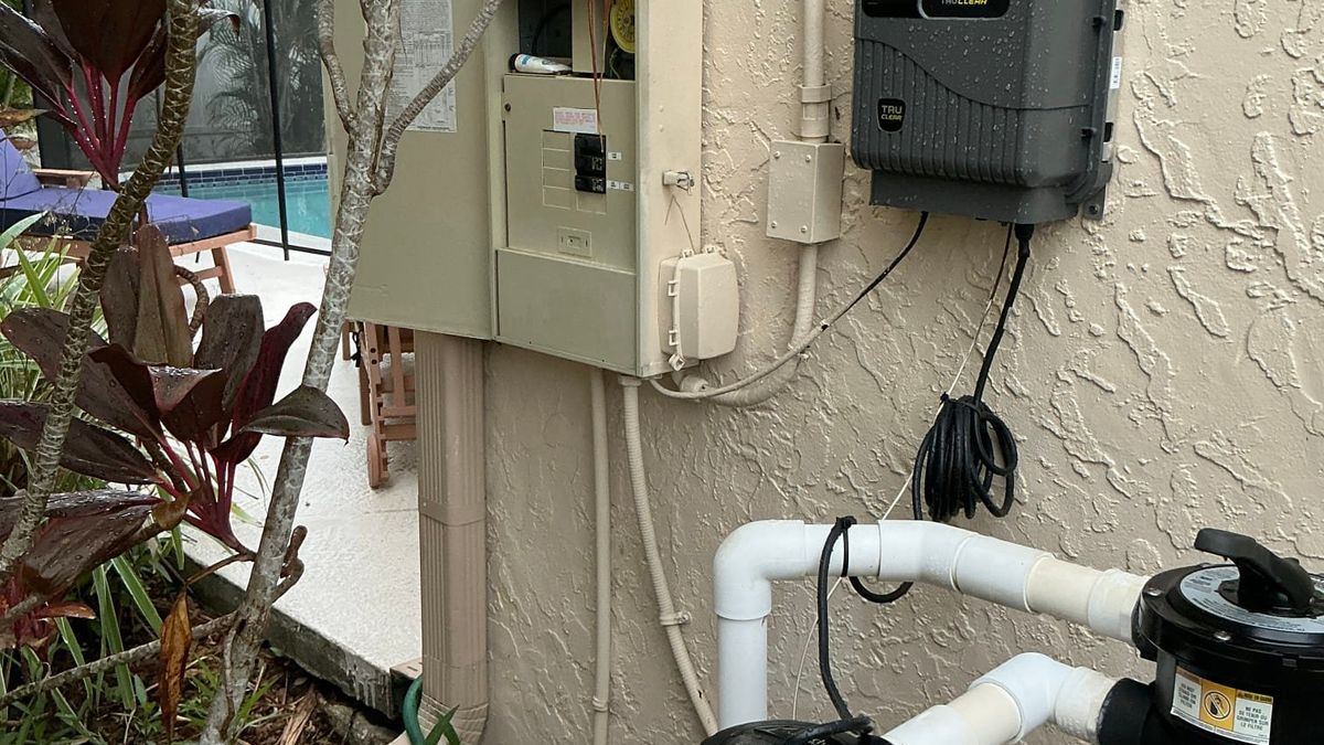 Pool equipment sub panel, disconnect and salt chlorine generator wired on a stucco wall beside a screened pool enclosure at a Palm Beach County home