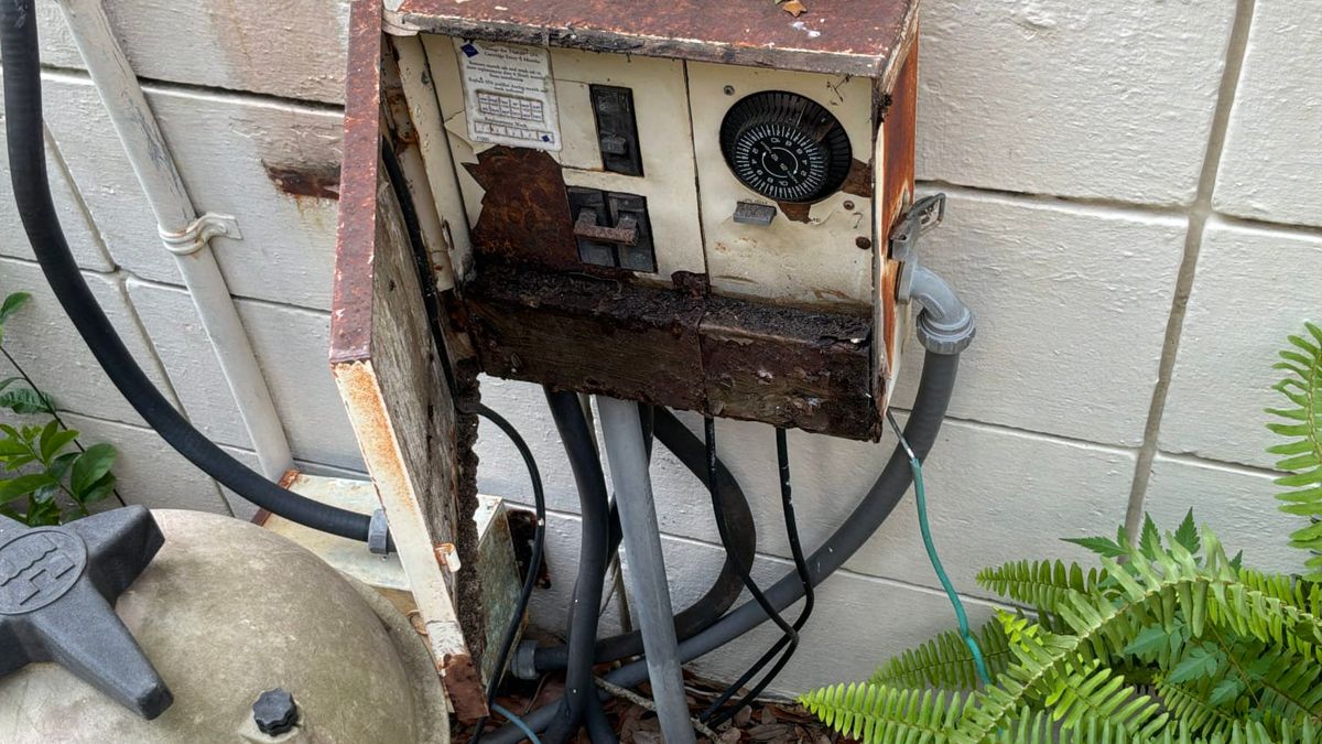 Rusted-through outdoor electrical panel enclosure on a concrete block wall at a coastal Palm Beach County home
