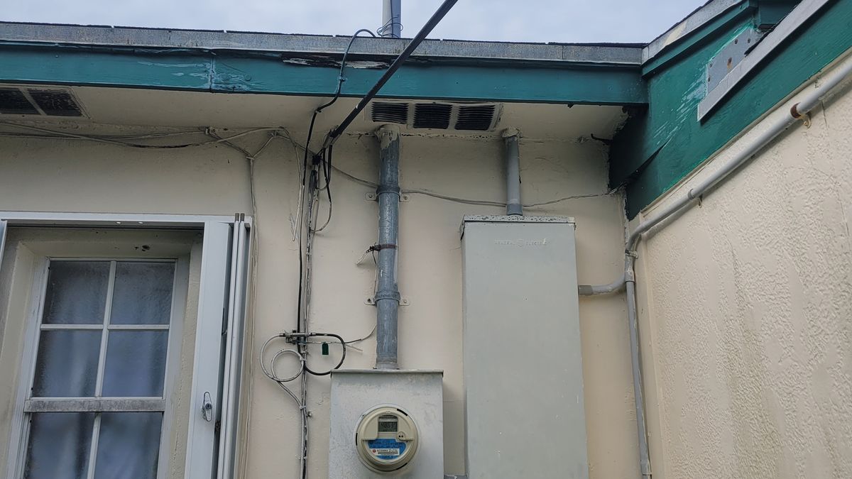 Service mast and riser running past the roofline to the overhead FPL service drop, with the meter enclosure below, on a Palm Beach County home